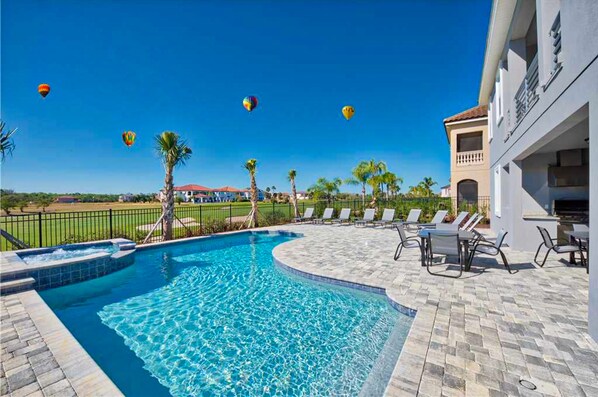Relax by the resort pool surrounded by lounge chairs and tables, with a low fence and palm trees nearby.