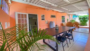Uma área de varanda interna com mesa, cadeiras, um dispensador de água e uma porta que dá para outro cômodo.