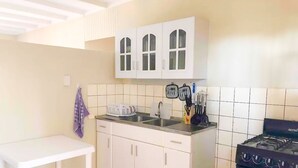 Uma cozinha pequena com armários brancos, uma mesa branca, uma pia e um fogão.