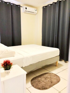 A bedroom with a bed, a small white table with a red flower, and a grey rug.
