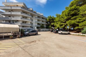 A multi-story parking structure with several cars parked, surrounded by trees and a building with balconies.
