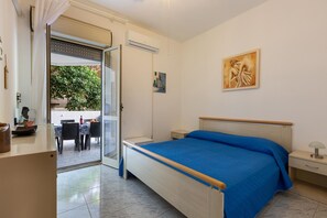 Ein Schlafzimmer mit einem Bett, einem Nachttisch, einem Schreibtisch, einem Stuhl und einem Fenster mit Blick auf Grünfläche.