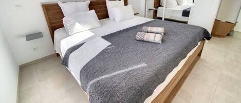 A neatly made bed with a patterned bedspread and pillows, a wooden headboard, and a white wall with a small shelf.