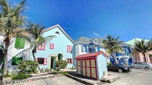 A two-story house with a red door, a small attached garage, and a garden with palm trees.
