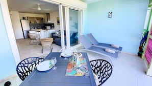 A dining area with a table set for two, a chair, and a view of the kitchen and living area through a glass door.