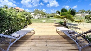 A wooden deck with two lounge chairs and a palm tree.