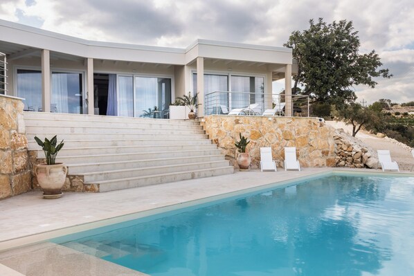 Una casa moderna con piscina, scale che conducono a un balcone e poltrona relax.
