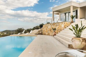 Ein moderner Poolbereich mit freiem Blick auf das Meer, einer Steinmauer und einer Treppe zu einem Gebäude.