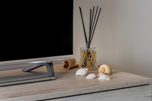 Un téléviseur à écran plat, un flacon en verre contenant des tiges de roseau et des coquillages disposés sur une surface en bois.