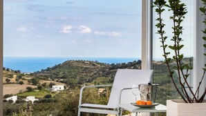 Ein Balkon mit einem weißen Stuhl, einem kleinen Tisch mit einem Glas Wasser und Orangen sowie einem Blumentopf.