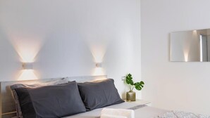 Ein modernes Schlafzimmer mit einem Bett, zwei Nachttischlampen, einer Topfpflanze und einem Wandspiegel.