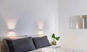 A modern bedroom with a bed, two bedside lamps, a potted plant, and a wall-mounted mirror.