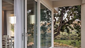 Ein Zimmer mit einer Schiebeglastür, die auf einen Balkon mit Blick auf einen Baum und die Landschaft führt.