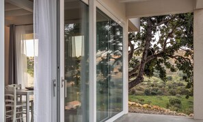 A room with a sliding glass door leading to a balcony with a view of a tree and landscape.