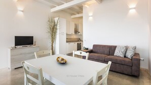 Ein modernes Interieur mit Esstisch, Stühlen, einer Couch, einem Fernseher und einer Küchenzeile.