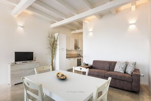 A modern interior with a dining table, chairs, a sofa, a TV, and a kitchen area.