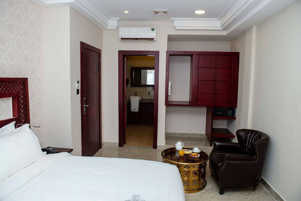 Habitación de hotel con cama, una silla, una mesita redonda con tetera y tazas, un armario y un equipo de aire acondicionado en la pared.