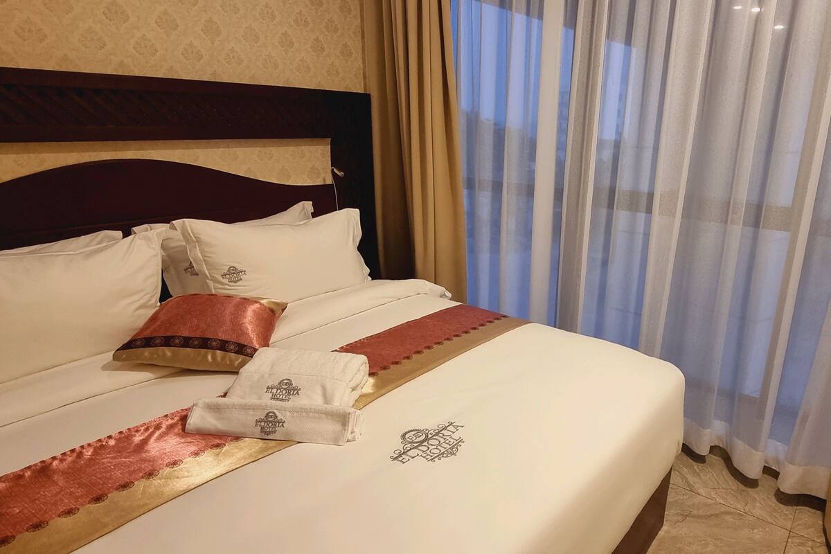 Una habitación de hotel con una cama bien hecha, un cabecero y un ventanal con cortinas.