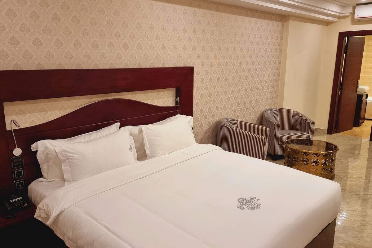 Habitación de hotel con una cama grande, cabecero de madera, teléfono y sillones a rayas.