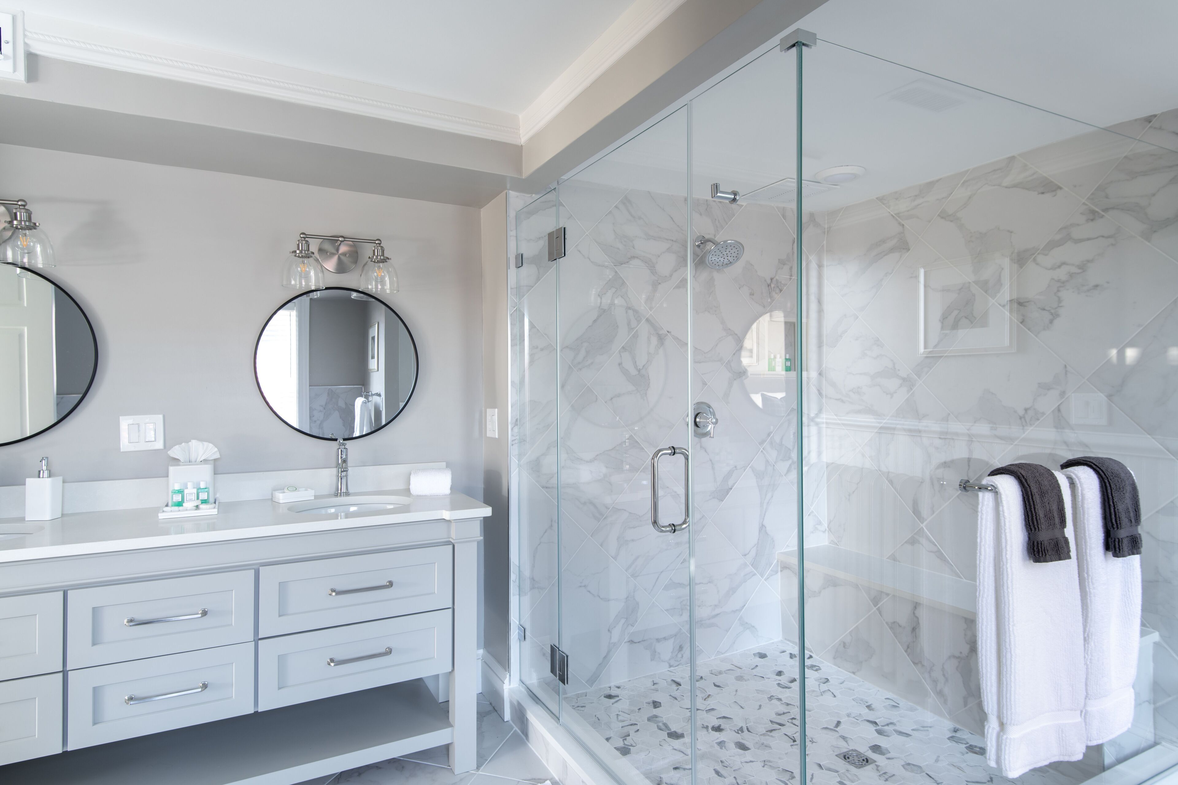 Une salle de bain moderne dotée d’une douche à parois de verre, de murs en marbre et d’un meuble-lavabo blanc avec des tiroirs.