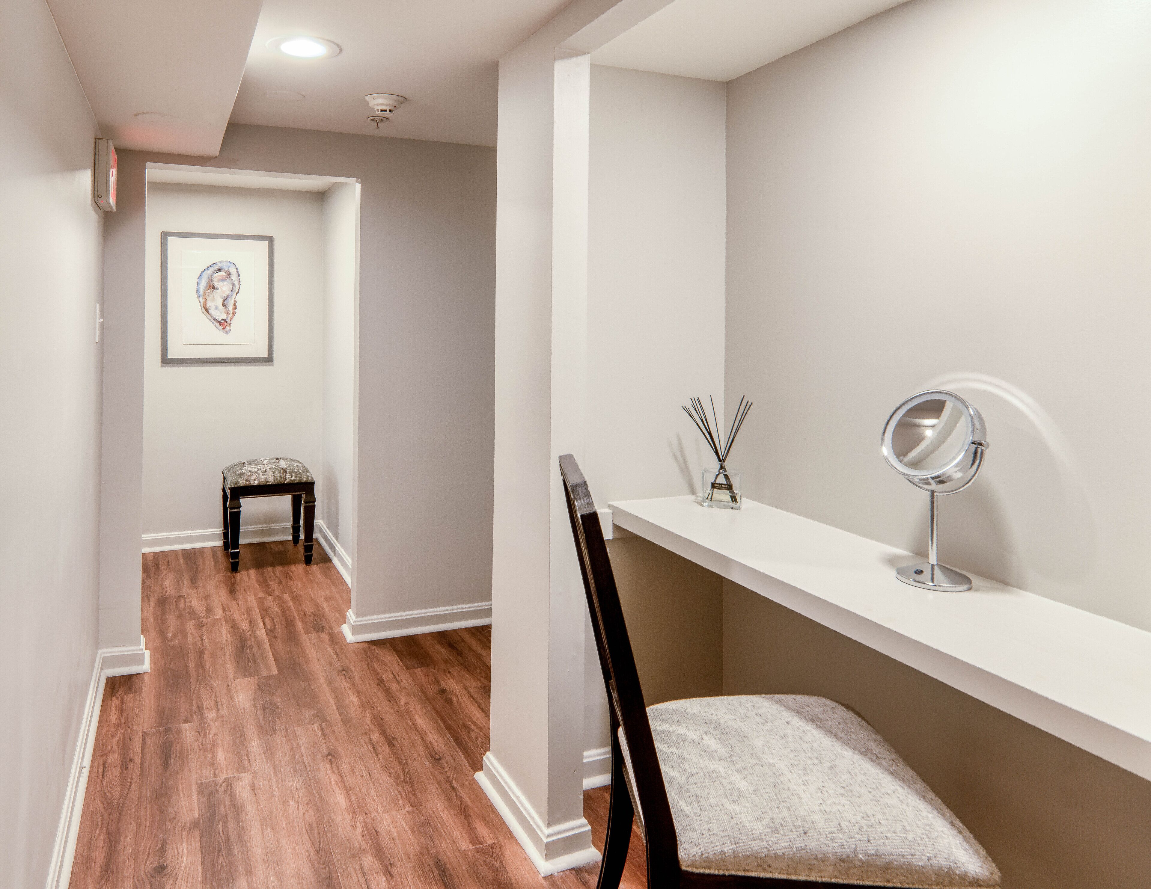 A hallway with a wooden floor, a bench, a framed artwork on the wall, and a vanity with a mirror and reed diffuser.