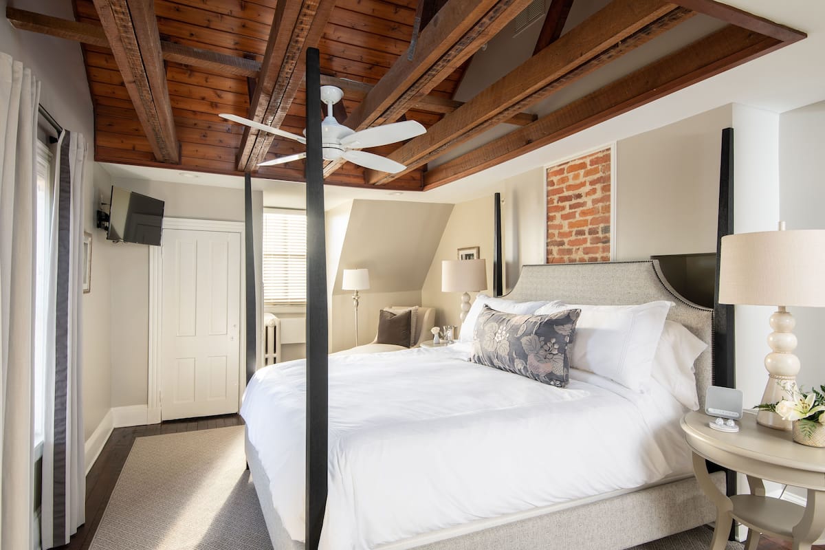 Un dormitorio con una cama grande, un ventilador de techo, una pared de ladrillo y una mesita de noche con una lámpara.