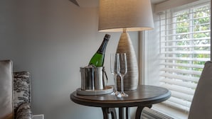 Una mesa con una botella de champán y copas, una lámpara y un ventanal con persianas.