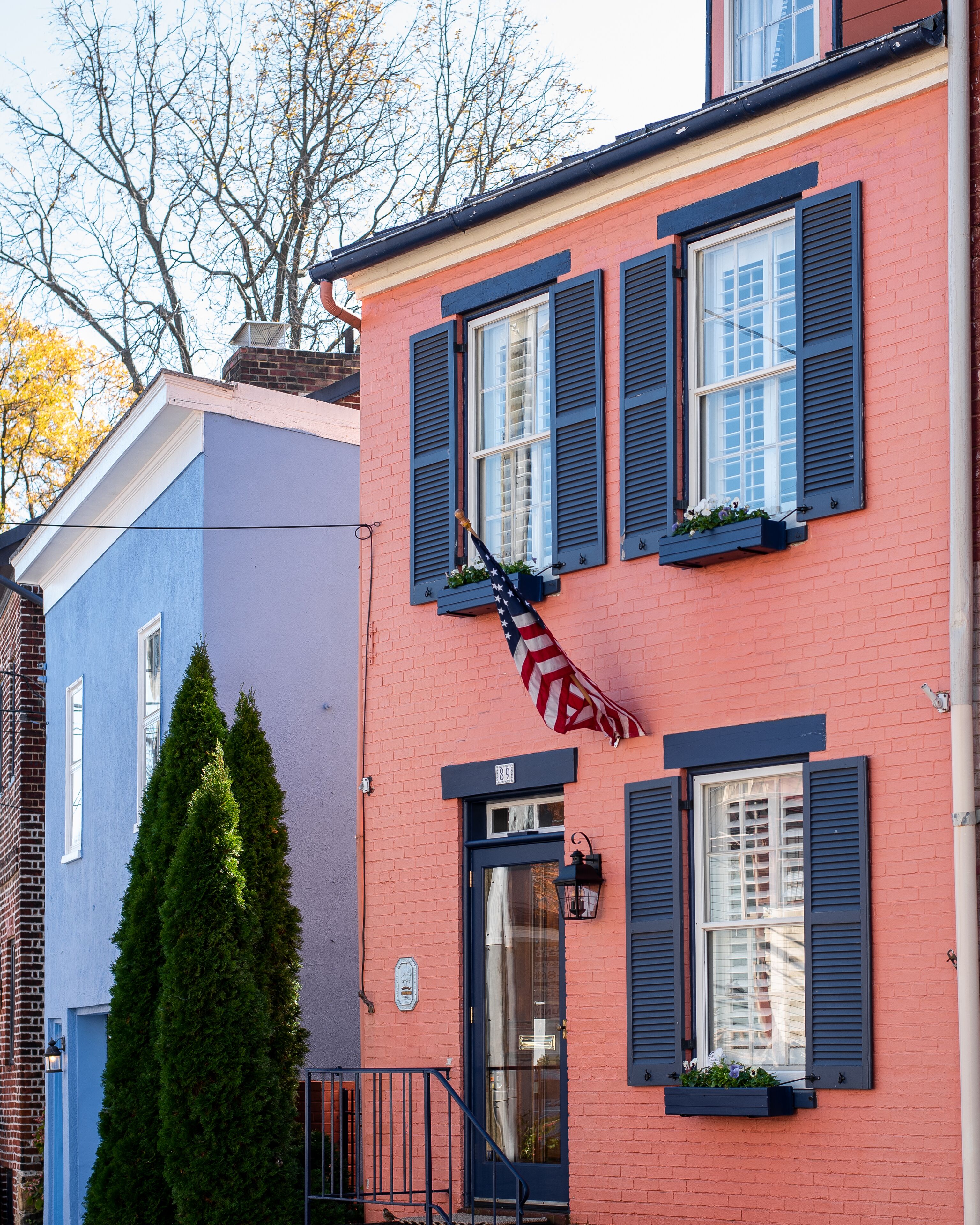 Una hilera de casas urbanas coloridas con fachadas azules y rosadas, contraventanas negras y una bandera.