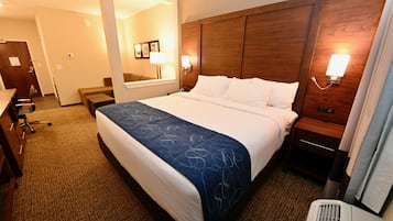 Habitación de hotel con una cama grande, un escritorio, una silla, una mesita de noche, una lámpara y un espejo.
