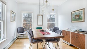 Ruokailutila, jossa on puinen pöytä, harmaalla kankaalla verhoillut tuolit ja riippuvalaisimet.