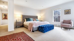 A bedroom with a large bed, two bedside tables, a blue ottoman, a chair, a window with a view of trees, and a rug. - Majestic estate in the mountains, over two acres of park-like land,... (Prattsville)