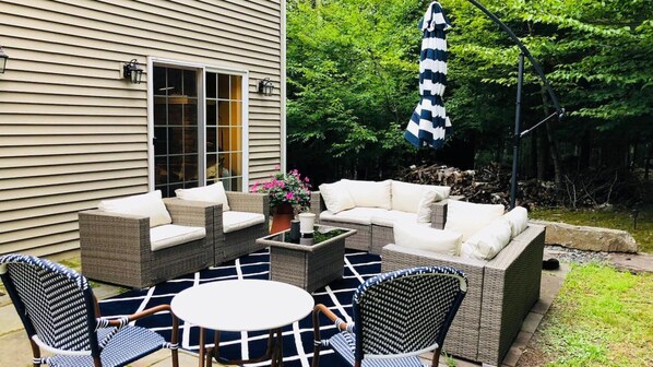 An outdoor patio with wicker furniture, a round table, and a striped umbrella. - Majestic estate in the mountains, over two acres of park-like land,... (Prattsville)
