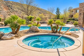 A pool area with multiple pools, surrounded by rocks and palm trees, set against a hilly backdrop. - Comfortable condo with indoor/outdoor pool (Hurricane)