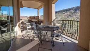 Une terrasse extérieure couverte, avec une table et des chaises, une porte vitrée et une vue sur un paysage désertique.