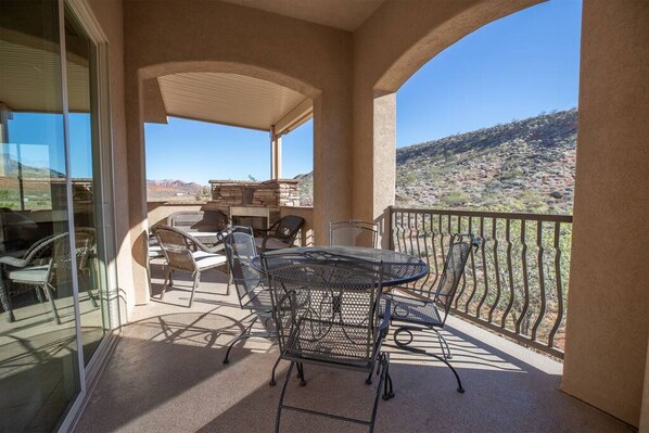 A covered outdoor patio with a table and chairs, a glass door, and a view of a desert landscape. - Comfortable condo with indoor/outdoor pool (Hurricane)