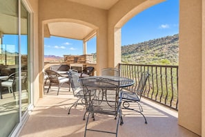 A balcony with outdoor furniture, a stone fireplace, and a view of a desert landscape. - Comfortable condo with indoor/outdoor pool (Hurricane)