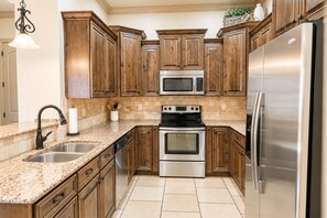 A kitchen with wooden cabinets, stainless steel appliances, granite countertops, and a tiled floor. - Comfortable condo with indoor/outdoor pool (Hurricane)