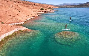 A clear lake with rocky terrain and two individuals paddleboarding.