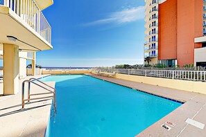 Relax by the pool with lounge chairs and umbrellas, surrounded by a white fence and overlooking the sea.
