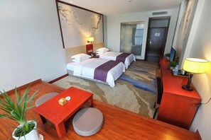 A hotel room with a bed, a desk, a chair, a table, a lamp, and a potted plant. - Bofei Hotel (Chongqing)