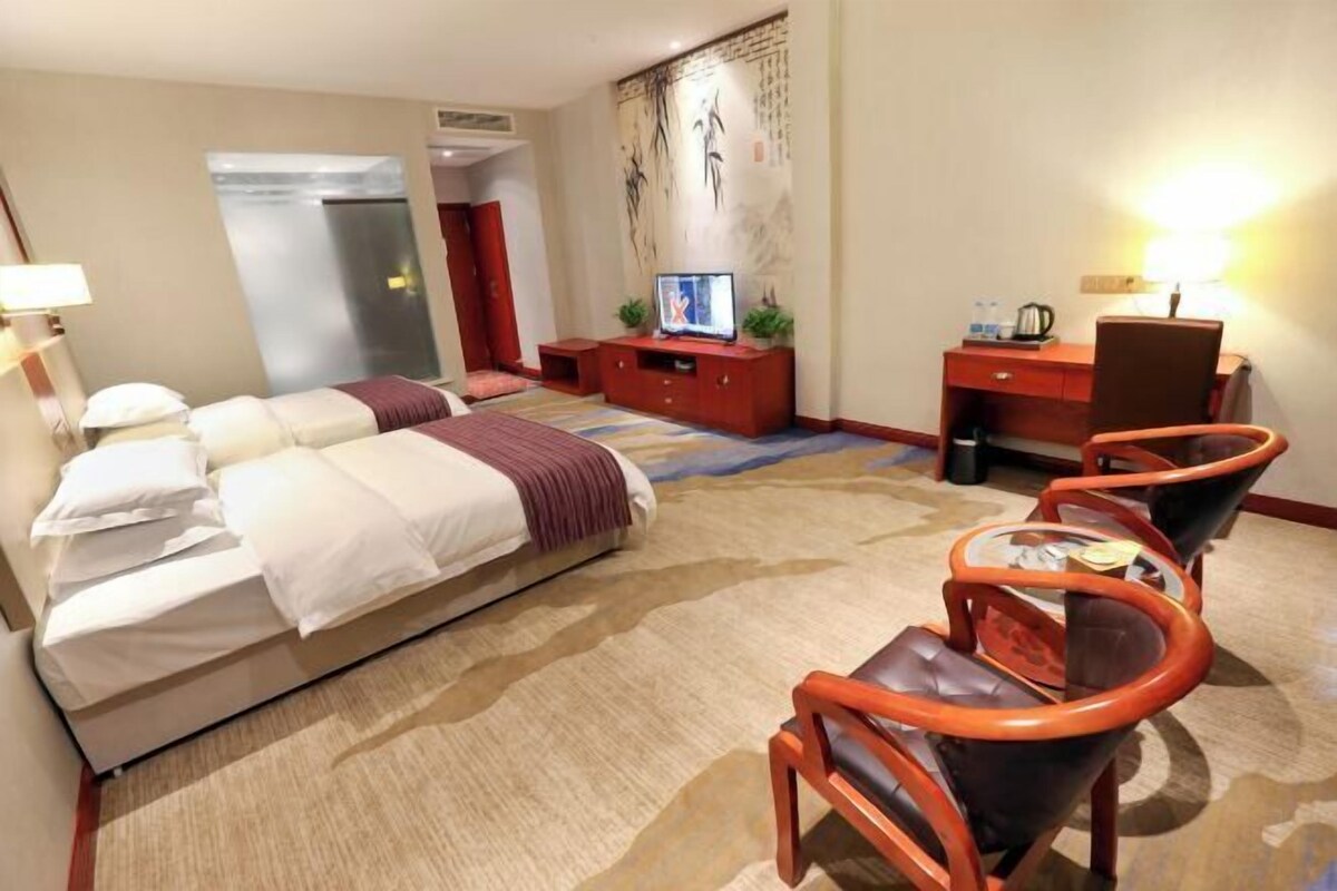 A hotel room with a bed, a desk, a chair, a television, and a wall with artwork.
