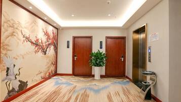 A hotel lobby with a traditional mural, two wooden doors, a potted plant, and an elevator.