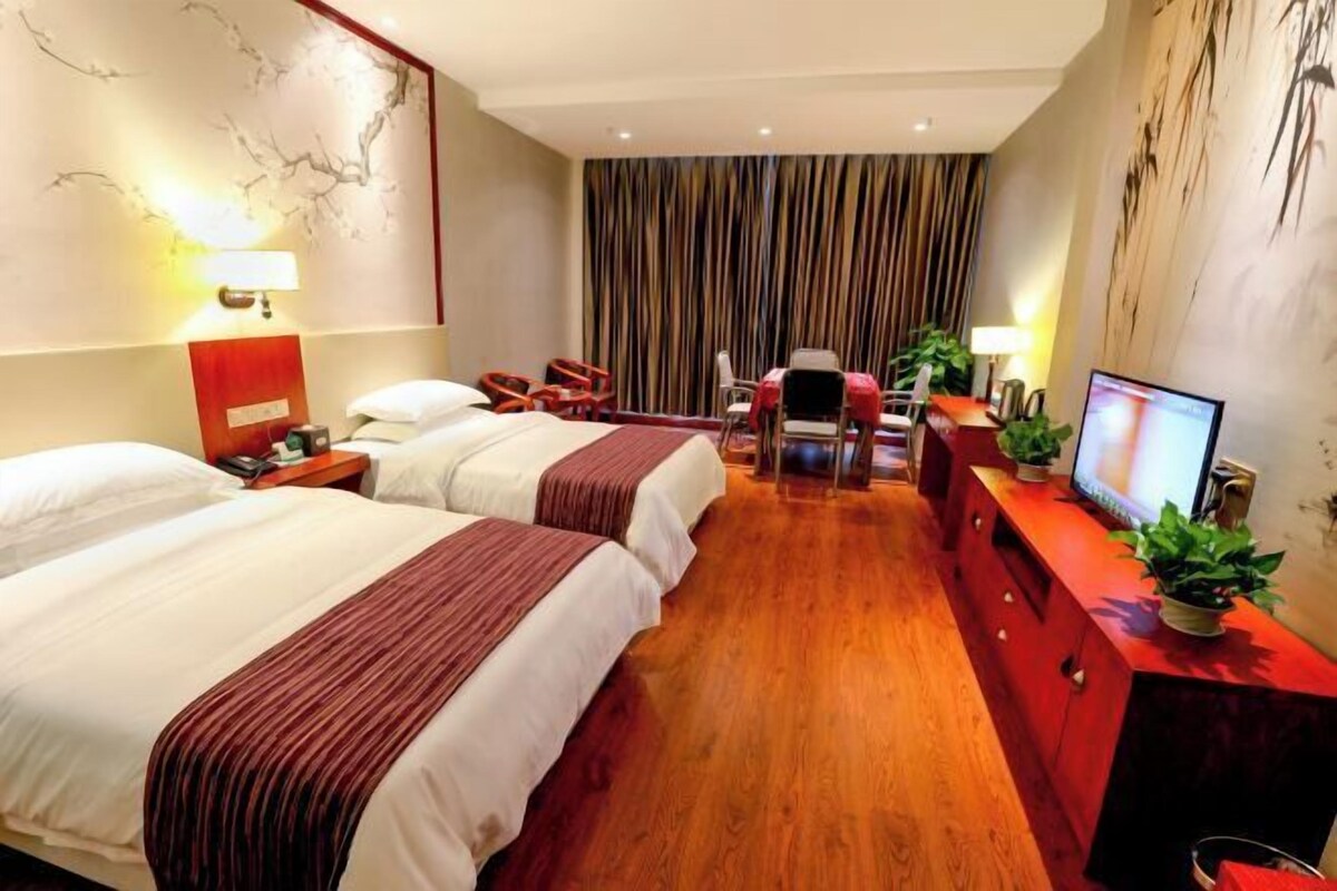 A hotel room with two beds, a desk with a computer, a TV, and a dining area with chairs.