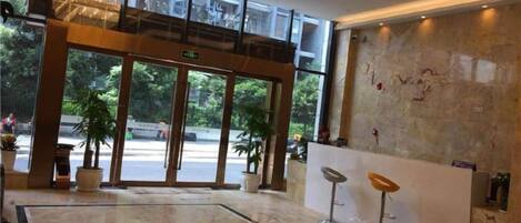 A hotel lobby with a glass entrance, a reception desk, and a seating area.