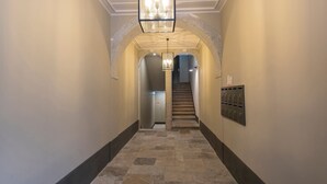 Ein Flur mit Steinboden, einer Treppe und einer Reihe von Briefkästen rechts.
