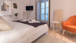 Ein Schlafzimmer mit Bett, Fernseher, Sessel und einer Tür, die auf einen Balkon führt.