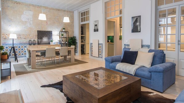 Un salon spacieux avec un canapé bleu, une table basse en bois et un coin repas comprenant une table et des chaises.