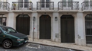 Ein Gebäude mit drei nummerierten Eingängen, ein grünes Auto davor und eine gepflasterte Straße.