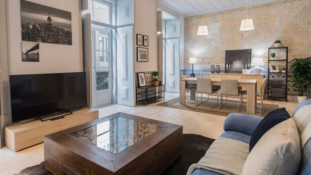 Ein modernes Wohnzimmer mit Flachbildfernseher, Glastisch, Sofa und Essbereich mit Tisch und Stühlen.