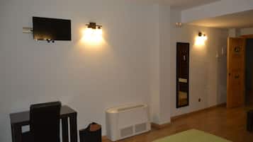Una habitación con cama, escritorio, silla, televisor montado en la pared y lámpara de pared.